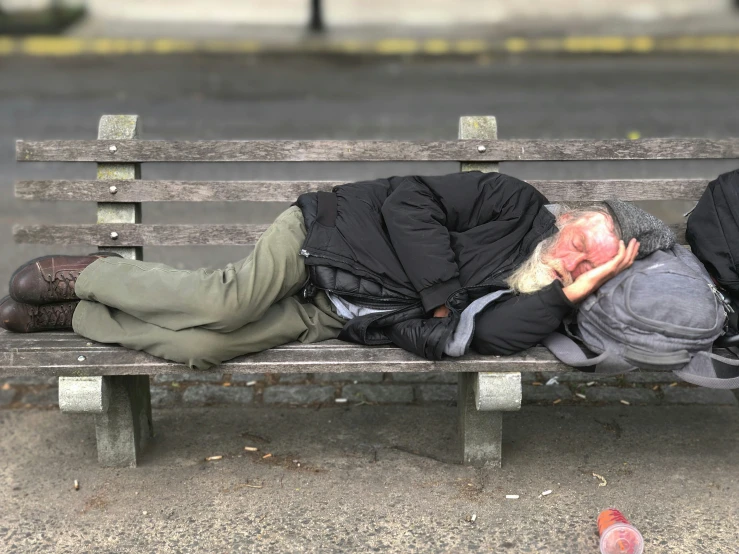 two homeless men nap on a park bench