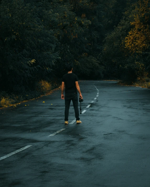 man with skateboard walking down the middle of a wet road