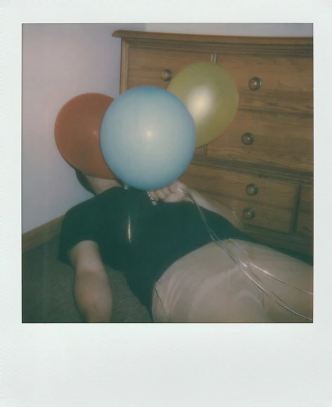 a person holding some balloons and sitting in the middle of a bed