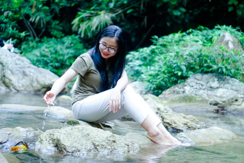 an asian woman is sitting on rocks in a creek