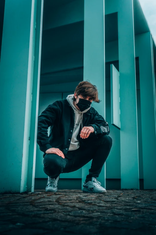 a man wearing face masks squatting in front of a blue wall