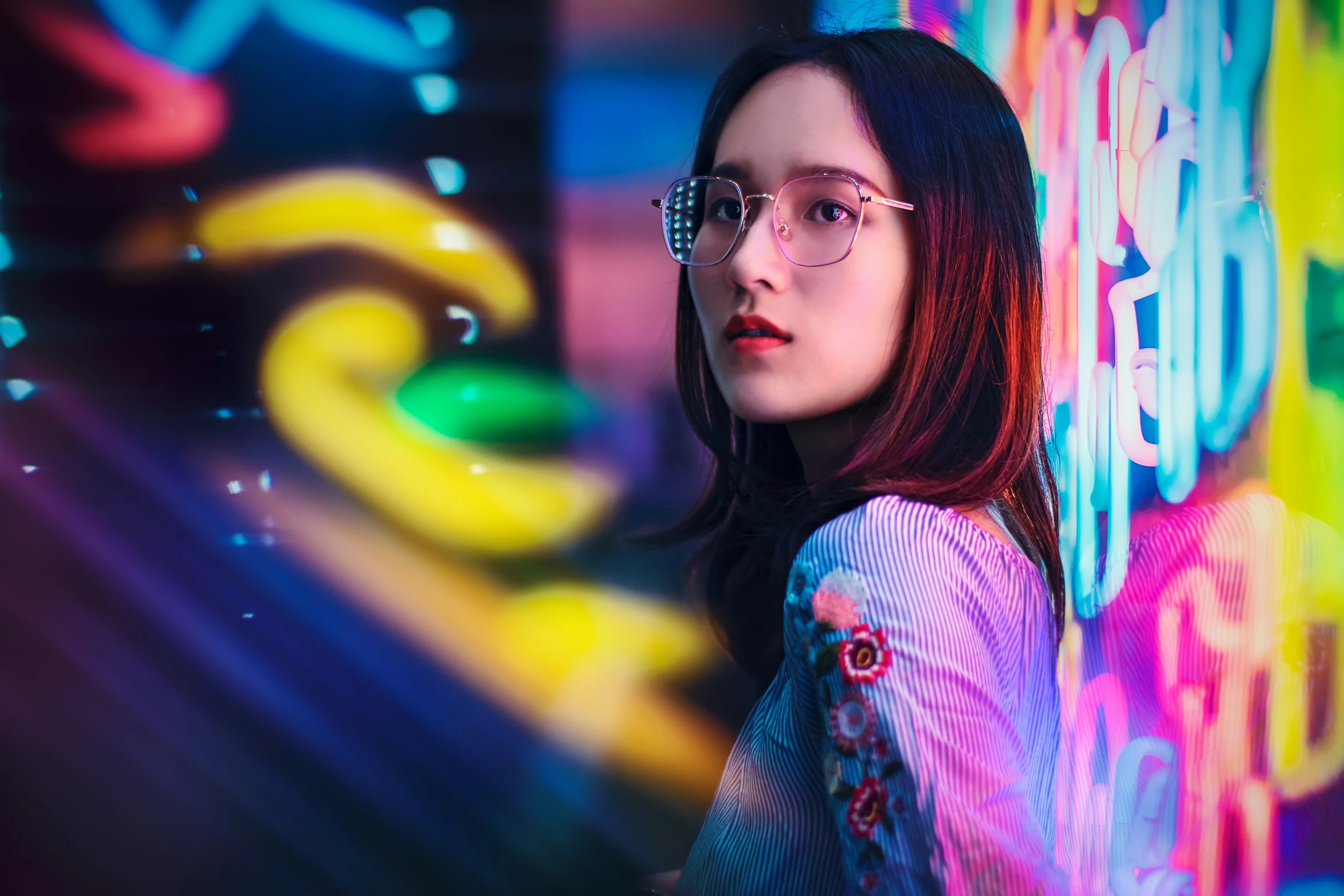 a girl in glasses posing against a wall with brightly colored graffiti