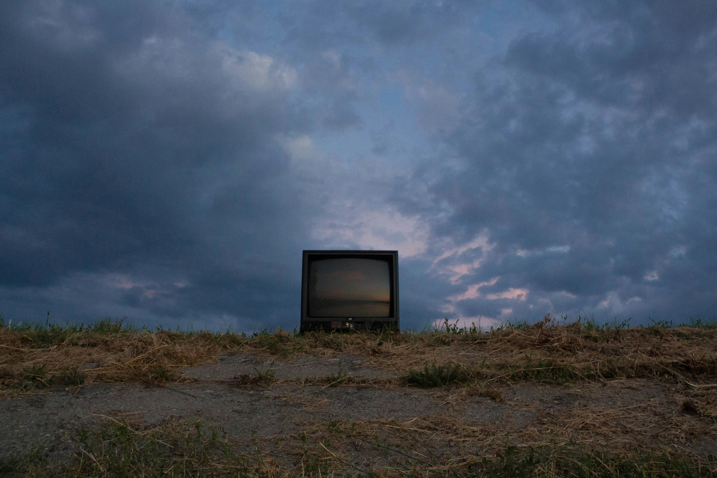 a tv that is sitting in the grass under a cloudy sky