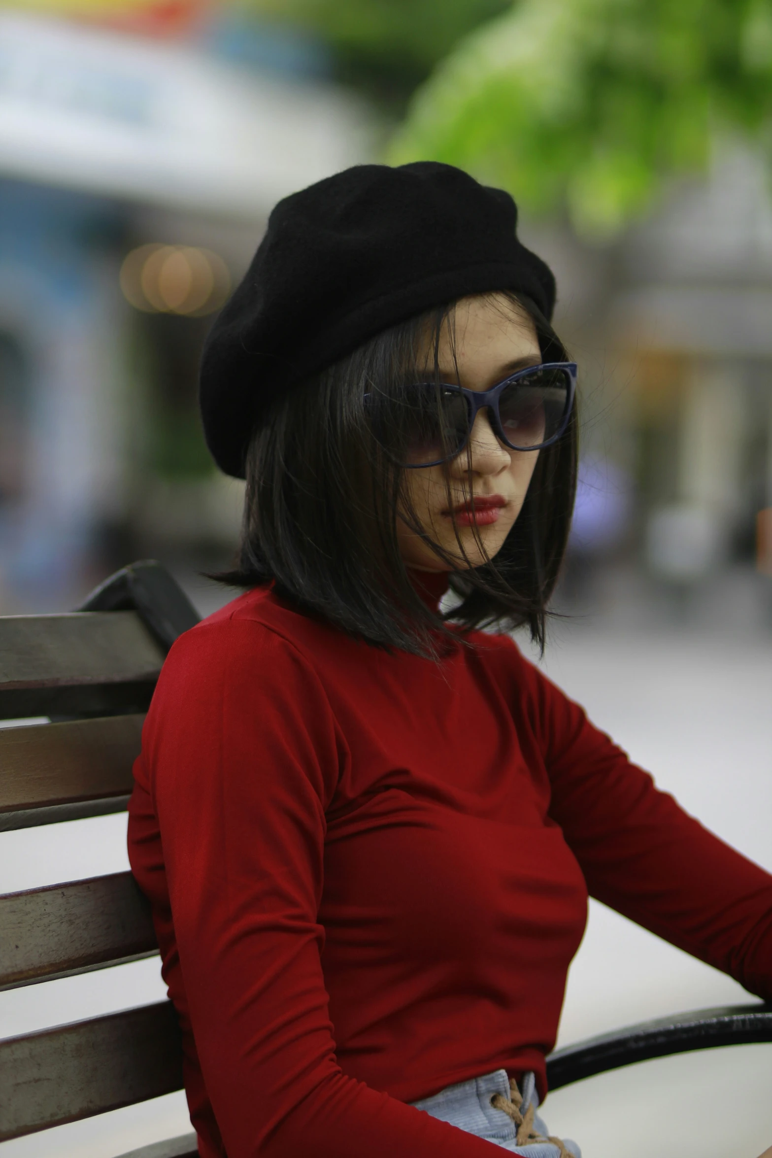 a woman wearing a hat and sunglasses seated on a bench