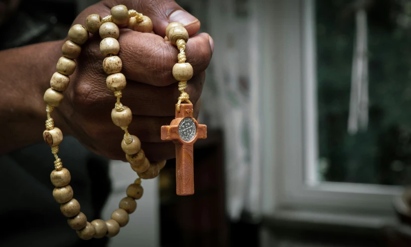 a man with a wooden rosary holding an ornate wooden cross