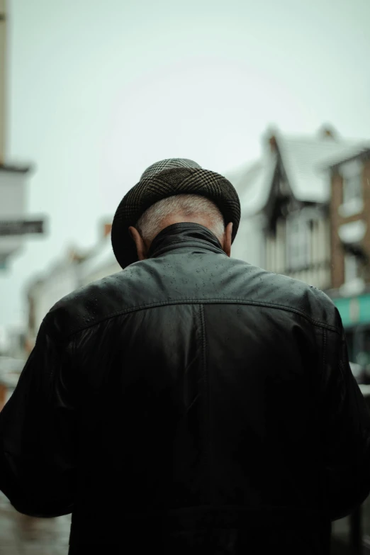 a man wearing a hat and black jacket walks down the street