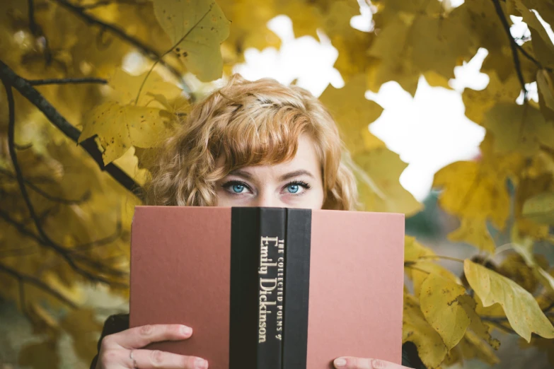 a woman with blue eyes is hiding behind a red book