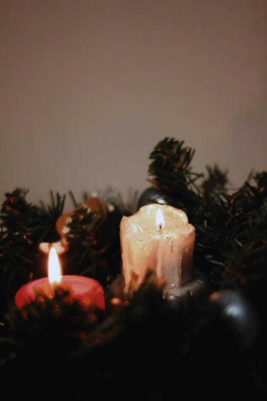 two candles sit beside pinecones and nches