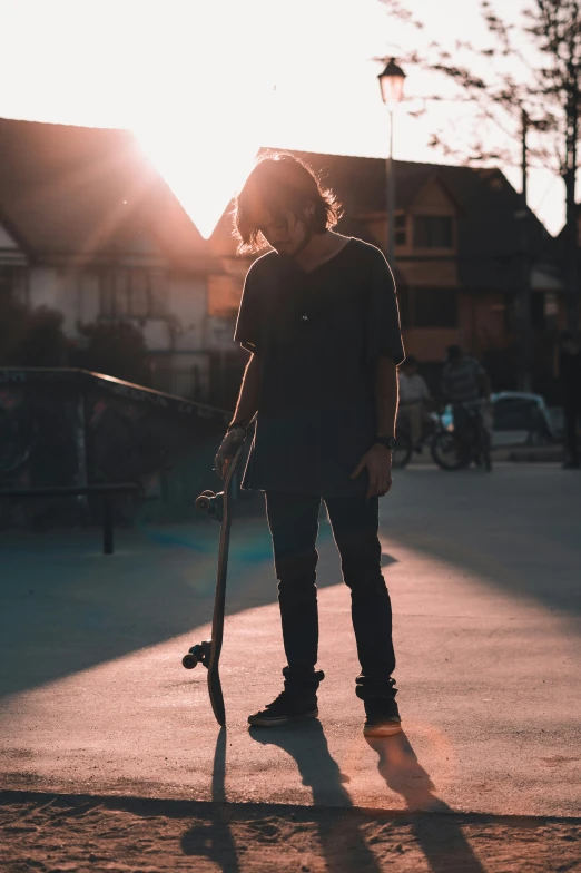 a man with long hair holds his skateboard on the sidewalk