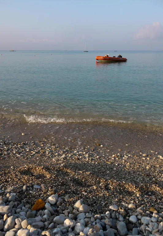 a small boat sits in the sea water next to shore stones