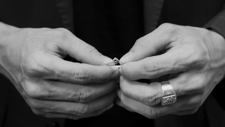 two hands hold a diamond ring, while another holds them