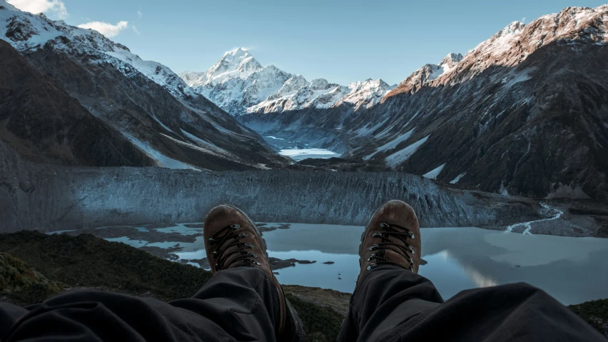 the view from a high altitude view point of a person's feet with their legs out, and mountains in the background