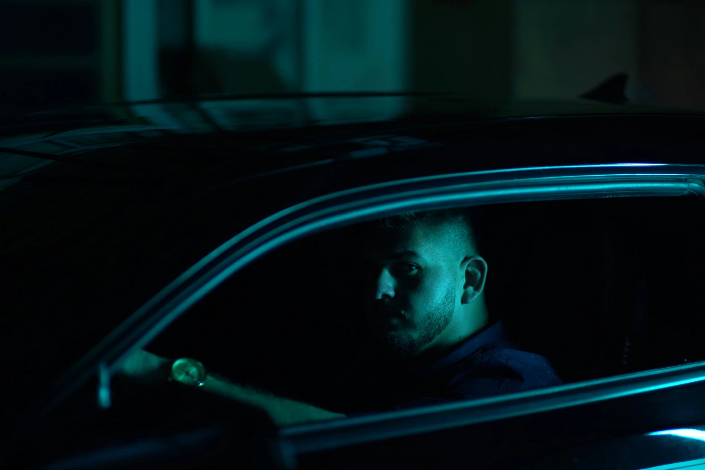 the man is in a dark car wearing a blue shirt