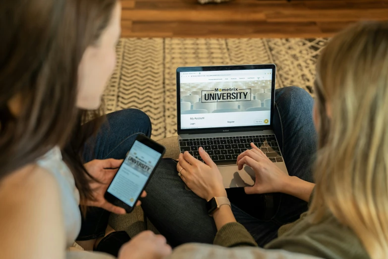 two women sitting on a couch looking at a tablet computer