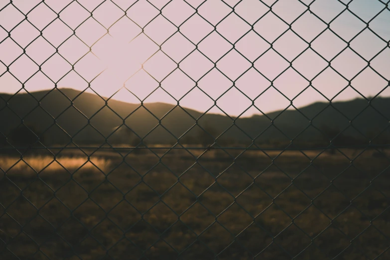 mountains behind a fence, with grass on it and water droplets on the fence