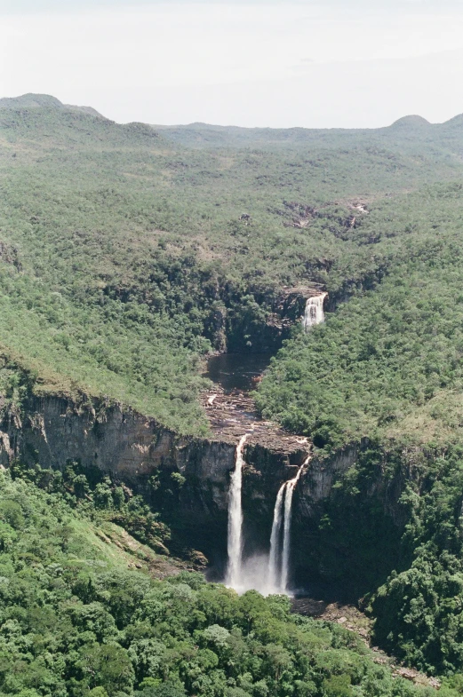 a waterfall in the middle of some trees and a lush green hill