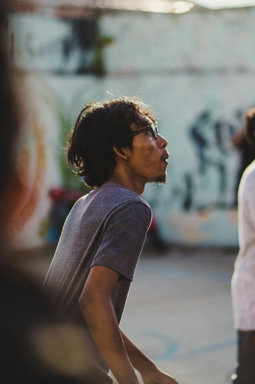 a young man wearing sunglasses watching other people on a tennis court