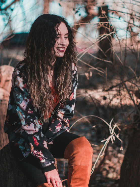 a woman wearing brown boots and a black floral shirt is sitting on a wooden fence