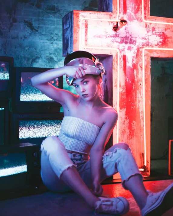 a young woman sitting on the floor with a glowing cross in the background