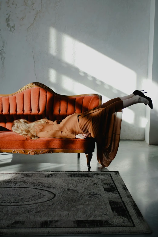 a woman in beige is laying on an orange couch