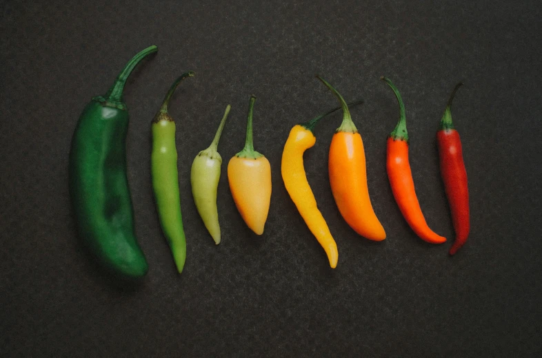 five orange and three green chili peppers on a black surface