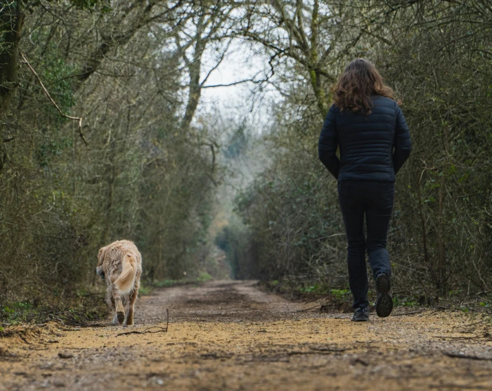 woman and her dog walking down the trail in the middle of a forest
