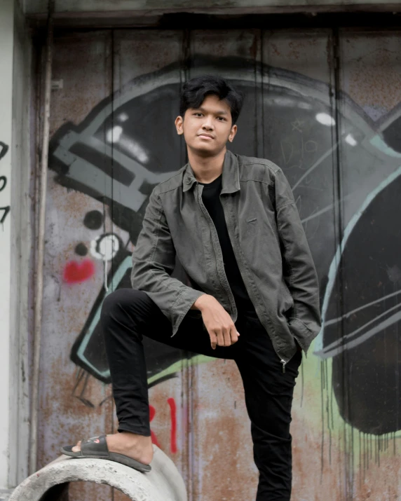 a boy poses on a concrete block in front of a wall with graffiti