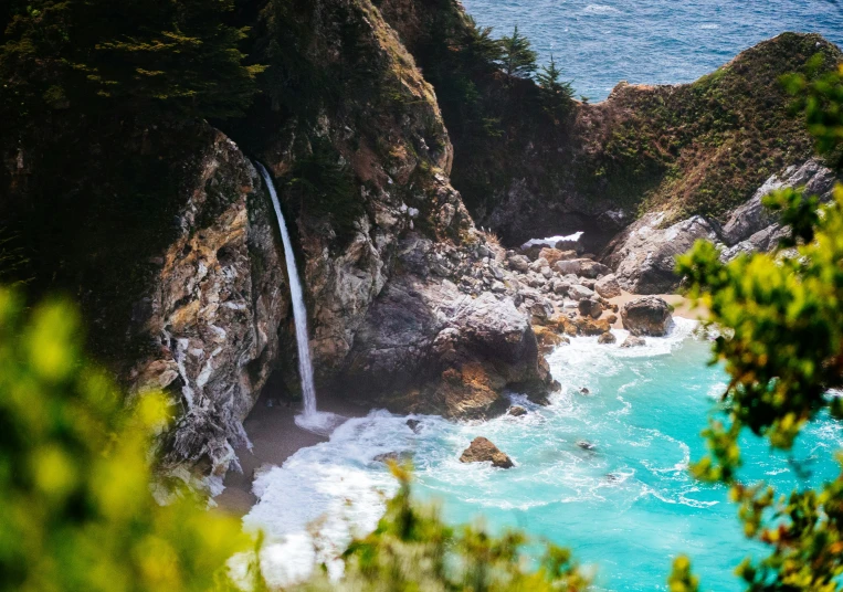 a waterfall on a cliff next to blue water