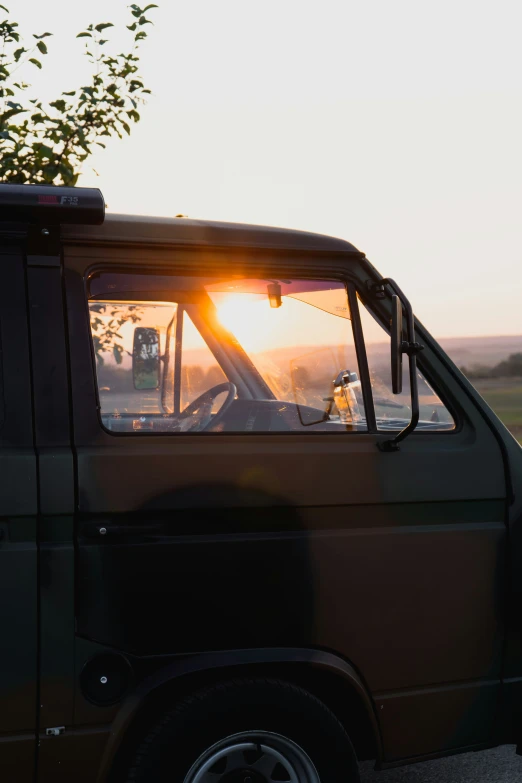 an old truck with a tree and the sun setting