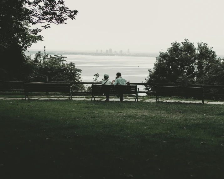 two people sitting on a bench looking at the water