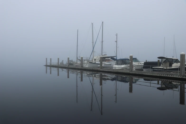 several sail boats sitting at a dock on a foggy day