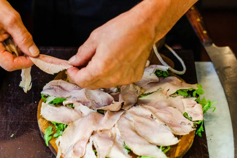 the hands are slicing the meat off of the deli board