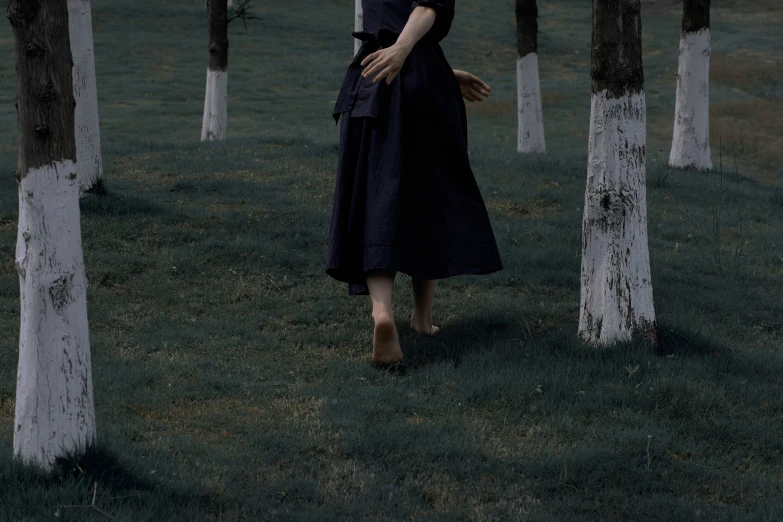 a girl wearing a hat stands in the grass between two tall trees