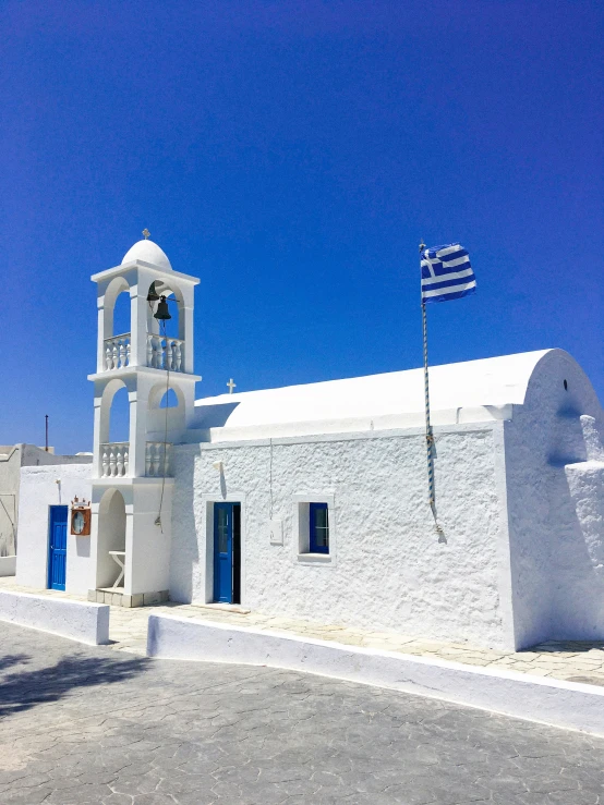 a small white building with an arched bell tower, with an american flag flying in the sky