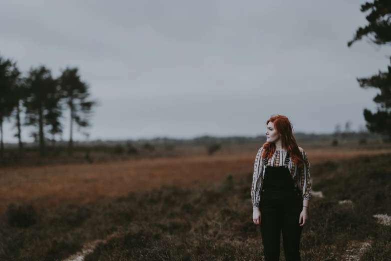 a woman stands alone in the middle of an open field with trees