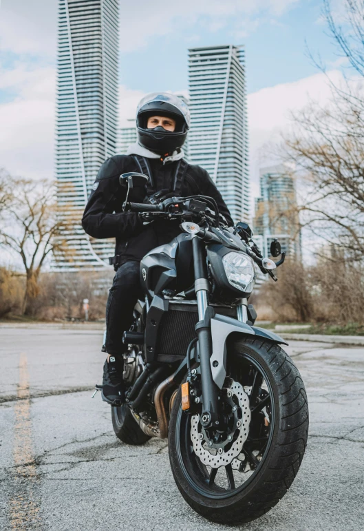 the man is posing with his motorcycle in front of two large buildings