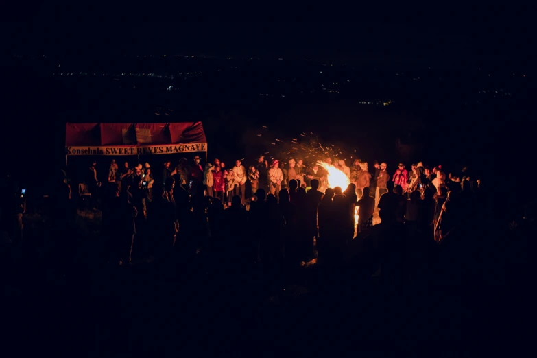 a big group of people standing around a fire pit at night