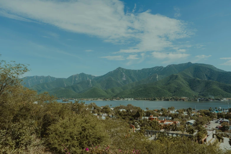 a city in front of mountains, water and trees