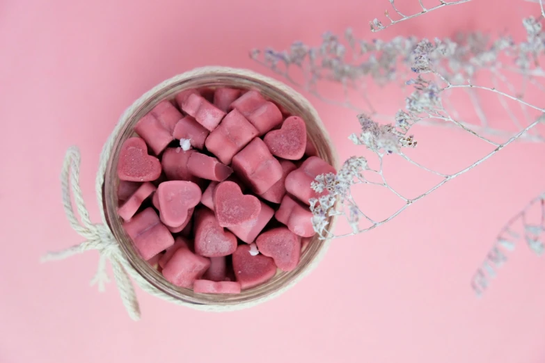 small hearts are in a woven basket on a pink background