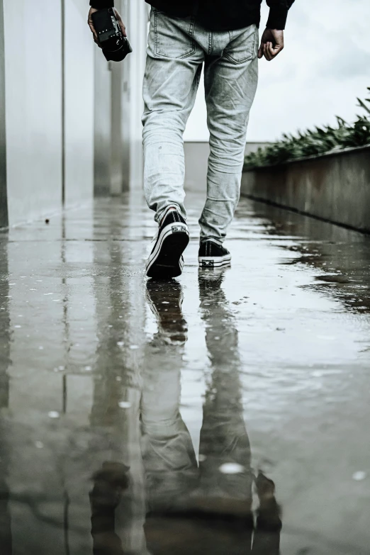 the man walks on a wet sidewalk holding an umbrella