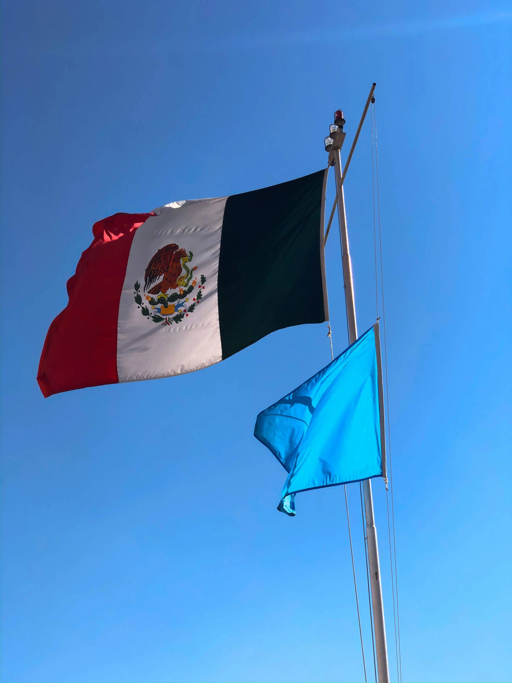 the mexican flag and green and white flag flutter next to each other