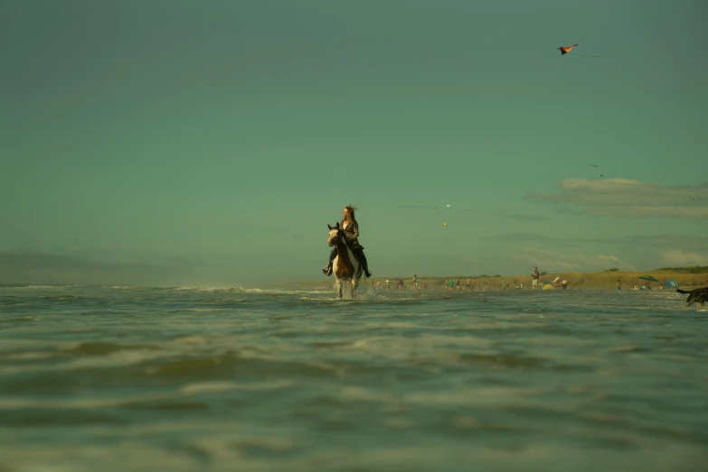 man riding horse through calm water and flying a kite