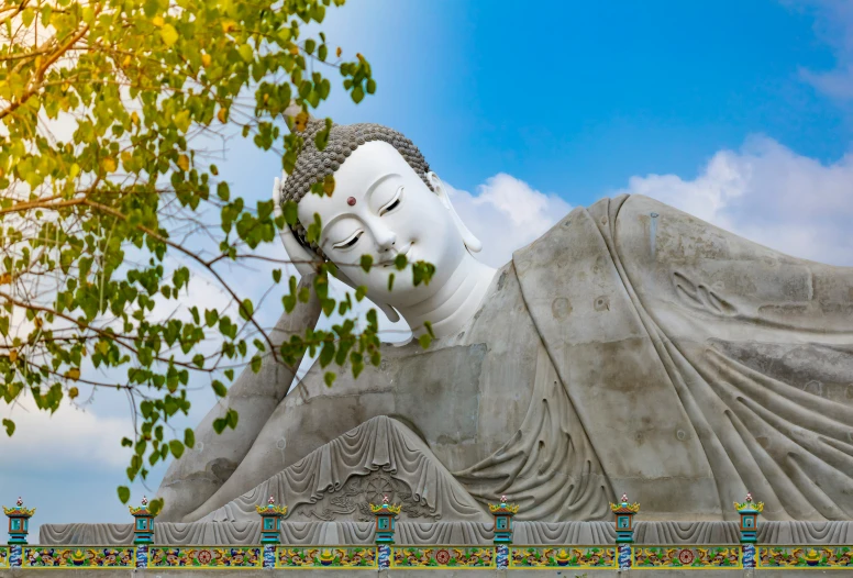 a large white buddha sitting in front of some trees