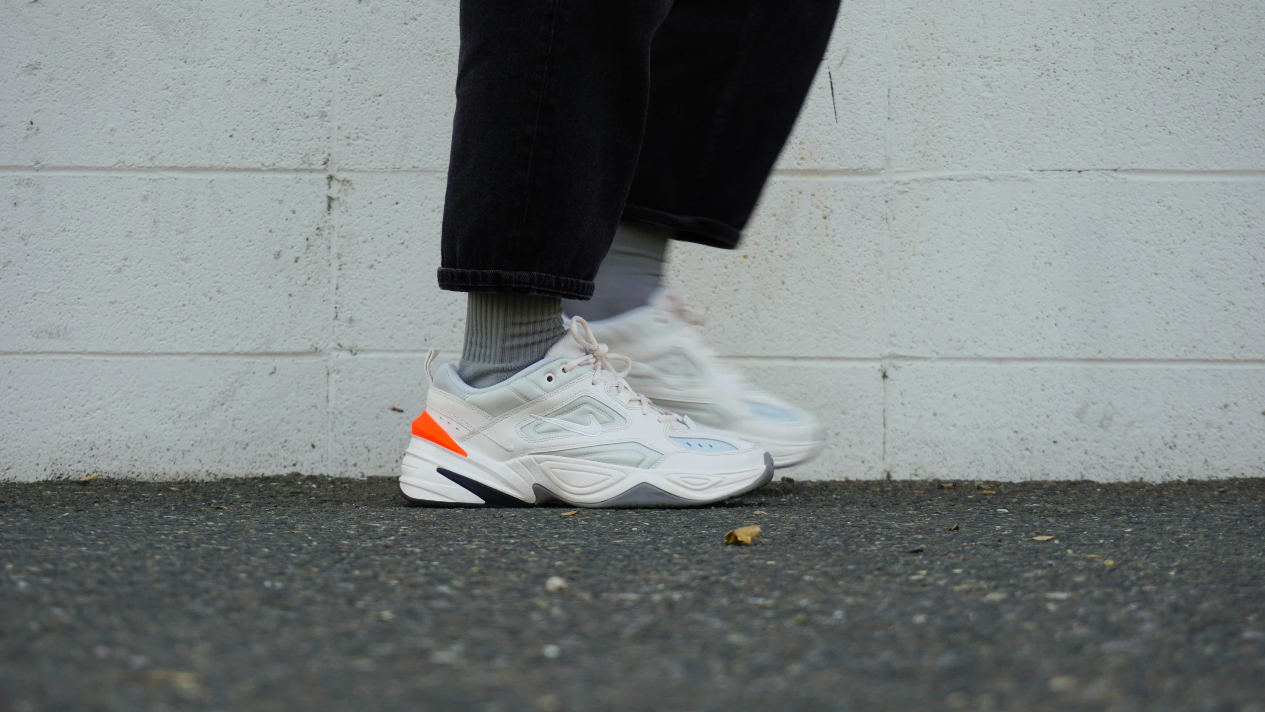 a person standing by the wall wearing white and orange sneakers