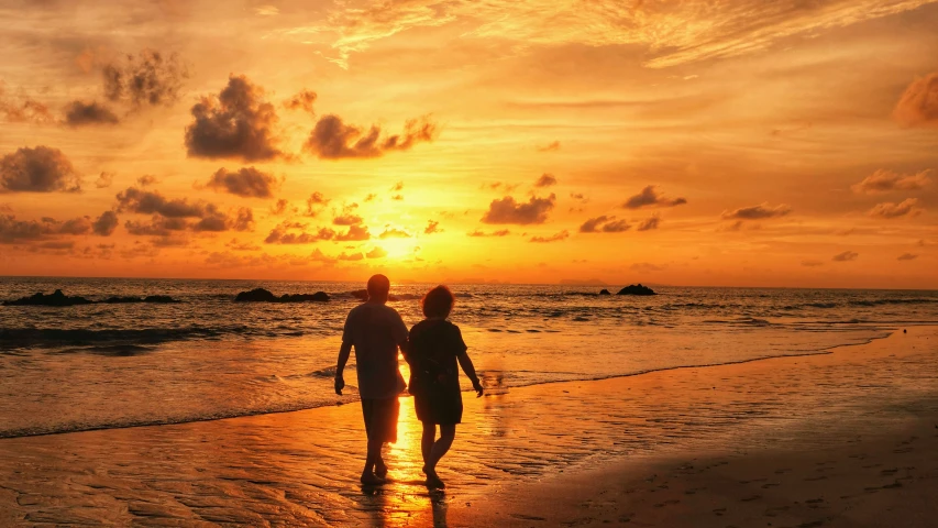 a couple walking towards the sunset on the beach