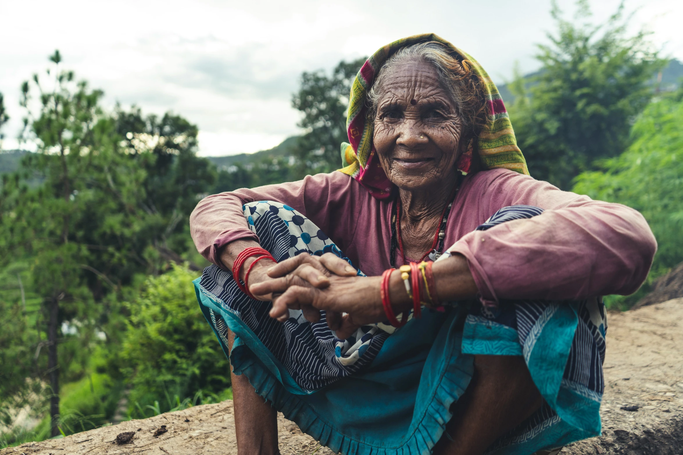 a woman with the traditional clothing on smiles while seated in the grass