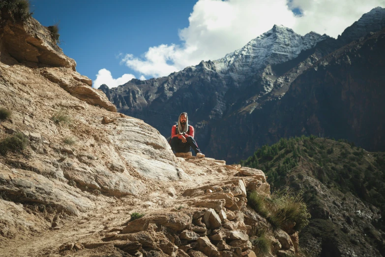 a man sitting on a rock by some mountains