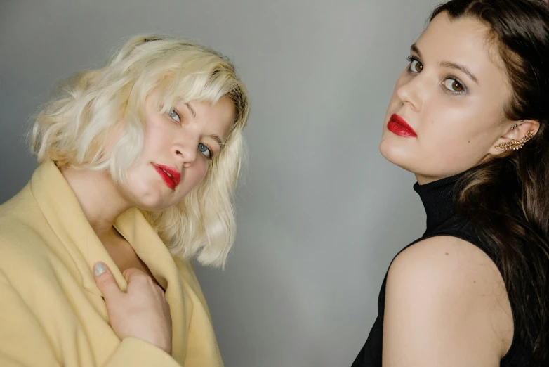 two women, one with short hair and red lips, looking opposite directions