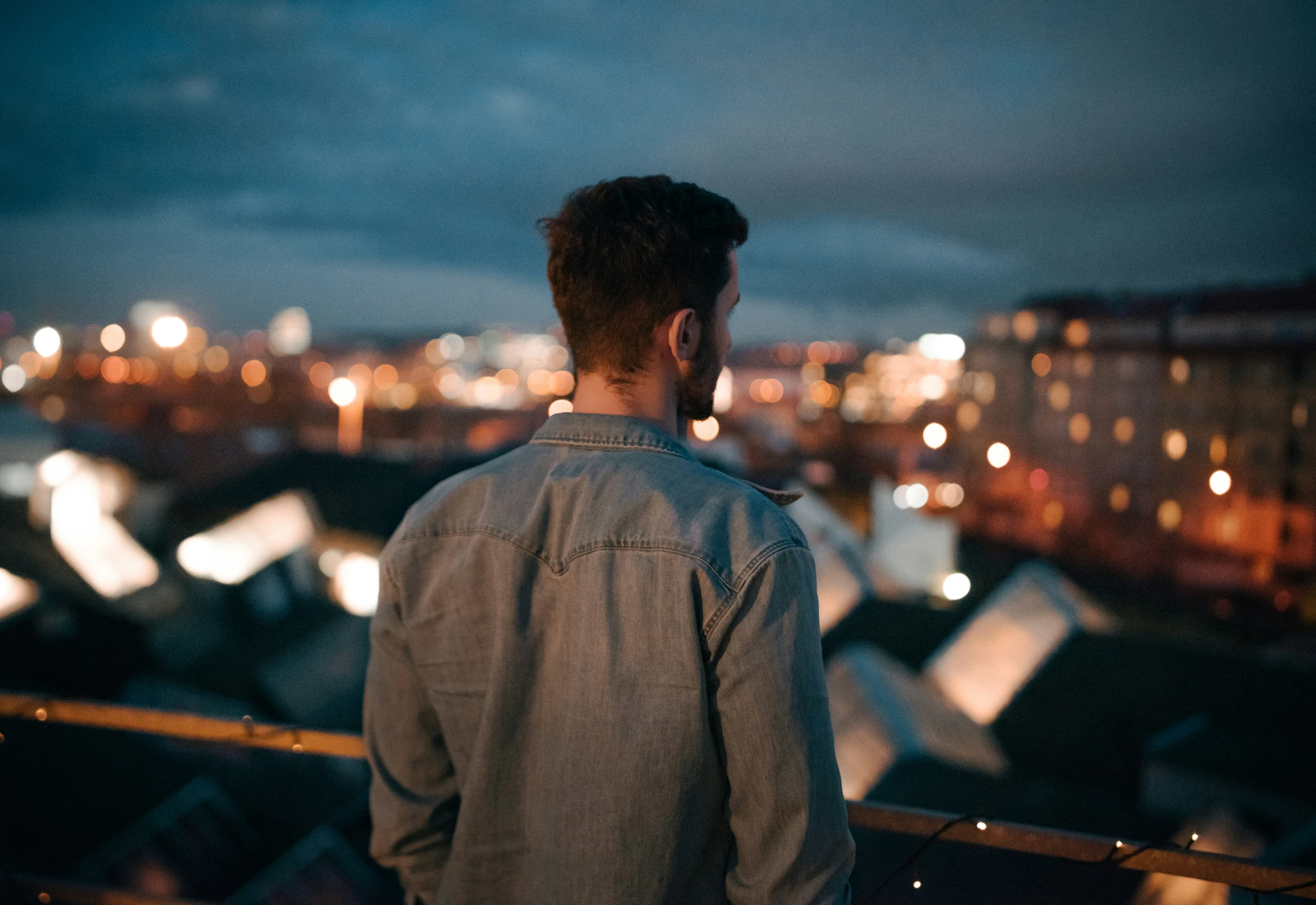 man standing outside looking at city lights and trees