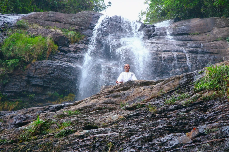 a man sitting on a rock under a waterfall